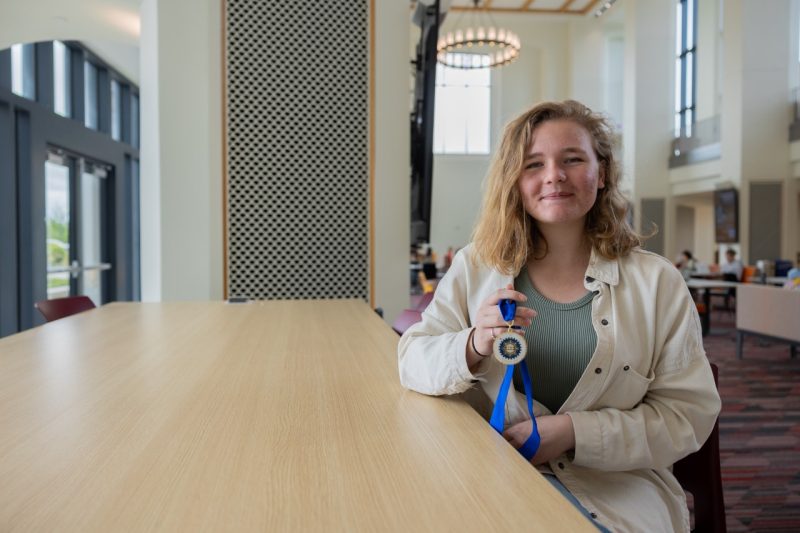 Abigail Dillard holds up her Phi Kappa Phi medallion in the Data and Decision Sciences Building. 