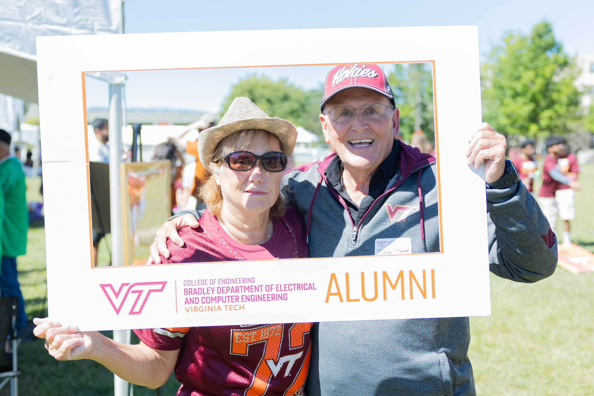 Two Virginia Tech ECE alumni pose with an alumni photo frame at a tailgate.