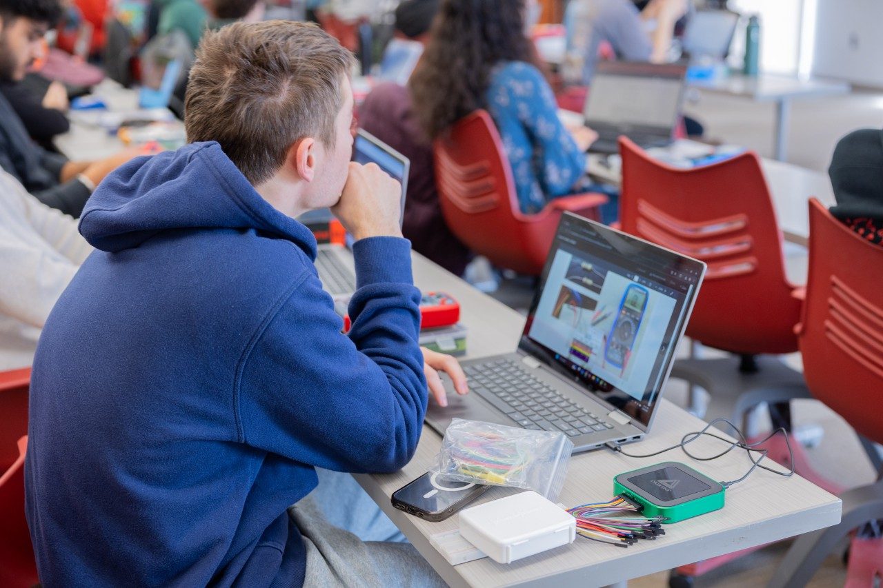 A student wearing a blue hoodie works on their laptop with the AD3 open next to it.