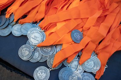 HLB Medals arranged on a table. Each medal has one side with the VT logo and one with the HLB logo. Each medal has an orange sash.