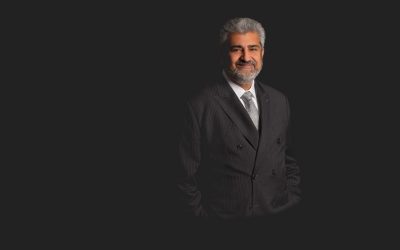 Ajay Jagtiani stands in a black suit against a black background. Photo courtesy of Ajay Jagtiani.