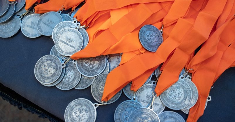 HLB Medals arranged on a table. Each medal has one side with the VT logo and one with the HLB logo. Each medal has an orange sash.